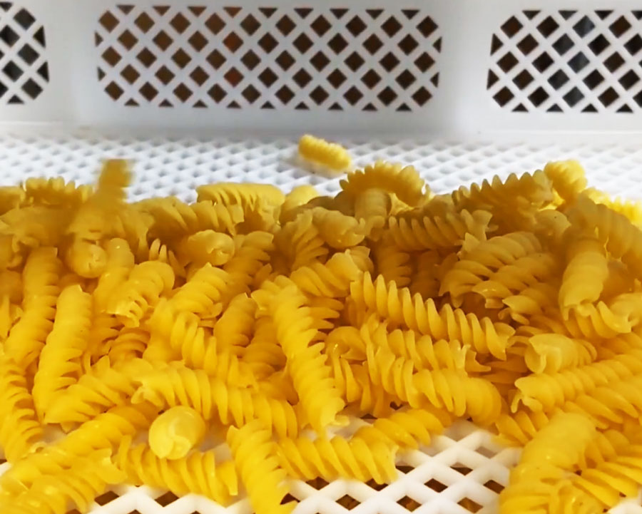 A pile of rotini pasta noodles sitting n a white pasta basket.